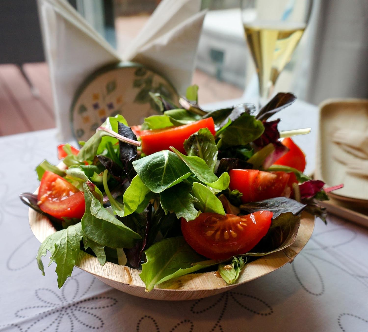 Green salad with tomatoes in a disposable palm leaf serving bowl